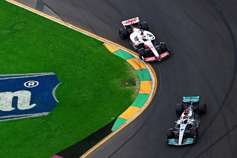 Imagem aérea mostrando a Haas branca e vermelha, de Kevin Magnussen, perseguindo a Mercedes prateada de George Russell em uma curva
