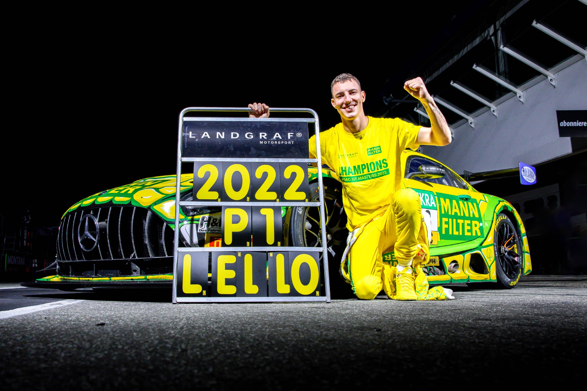 Raffaele Marciello, de camiseta amarela, na frente de uma Mercedes GT3 amarela, dando um soco para o alto e segurando uma placa escrita "2022, P1, Lello"